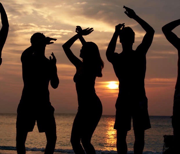 Drei Personen tanzen am Strand bei Sonnenuntergang